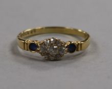 An early 20th century diamond cluster ring with sapphire set shoulders, size R.