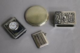 A silver compact, clock, vesta and matchbox cover.