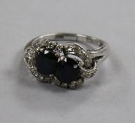 An 18ct white gold and two stone sapphire crossover ring with diamond set border, size N.