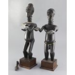 A pair of African ebonised wood figures of a man and woman standing with outstretched arms, on