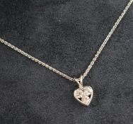 A platinum and three stone diamond set heart shaped pendant on chain.