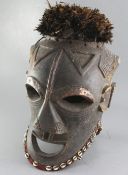 A large West African carved wood Janus helmet mask, decorated with cowrie shells and feathers,