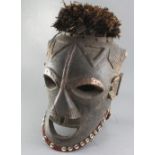 A large West African carved wood Janus helmet mask, decorated with cowrie shells and feathers,