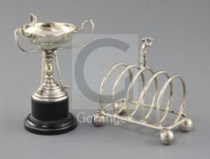 A 1940's golf interest silver toastrack surmounted by a golfer on golf ball feet by W.T. Wiseman,