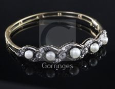 An Edwardian gold, pearl and diamond hinged bangle, set with five graduated pearls, divided by