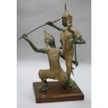 An Indonesian bronze group of two deities fighting, with gilt and green patination, on rectangular