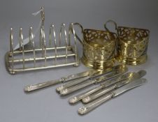 An Edwardian silver toastrack, two gilded white metal cup holders and six silver handles tea