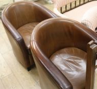 A pair of tub chairs covered in brown hide