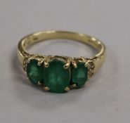 A 14ct gold, three stone emerald ring with diamond chip shoulders, size P.