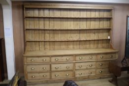 A large Victorian pine dresser, with three shelf rack and twelve long drawers, on plinth foot W.