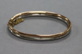 A yellow and white metal hinged bangle, with safety chain.
