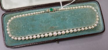 A single strand graduated cultured pearl necklace with an emerald and diamond set white metal clasp,