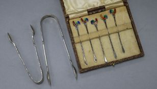 Five silver and enamel cocktail sticks and two pairs of silver sugar tongs.