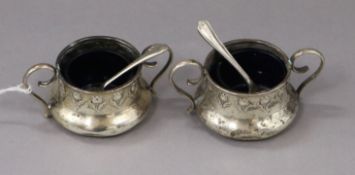 A pair of George V Art Nouveau silver two handled salts and two associated plated spoons.