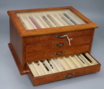 A burr wood four-drawer pen collectors' cabinet containing various pens, including Dunhill and