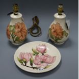 A pair of Moorcroft Hibiscus pattern table lamps and a Magnolia pattern plate, both decorated with