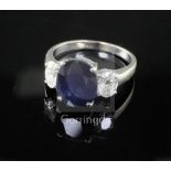 An 18ct white gold sapphire and diamond three stone dress ring, the oval cut sapphire weighing