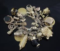 An early 20th century 18ct gold charm bracelet, hung with twenty seven assorted mainly 9ct gold