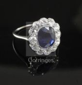 A white metal, sapphire and diamond oval cluster ring the central oval cushion cut sapphire bordered