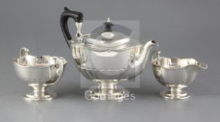 A George V silver three piece pedestal tea set, Alexander Clark & Co Ltd, with demi-panelled