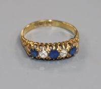 An Edwardian 18ct gold, sapphire and diamond five stone half hoop ring, size M.