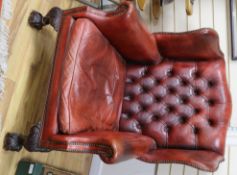 A George II style red leather buttoned wing armchair, ball and claw feet