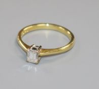 A modern 18ct gold and solitaire emerald cut diamond ring, the stone weighing approximately 0.25cts,