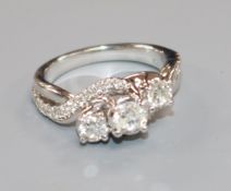 A modern 14k white gold and three stone diamond crossover ring with diamond set shoulders, size N.