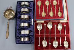 Two cased sets of silver spoons, a cased set of six silver napkin rings and a silver tea strainer on