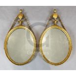 A pair of George III giltwood and gesso oval wall mirrors, with urn and bell husk crests, W.1ft 5in.