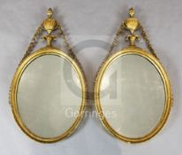 A pair of George III giltwood and gesso oval wall mirrors, with urn and bell husk crests, W.1ft 5in.