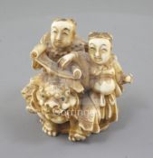 A Japanese ivory okimono of two boys with a Buddhist lion, Meiji period, both holding a scroll,