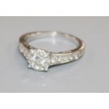 A modern white metal and diamond cluster ring with diamond set shoulders, size I.