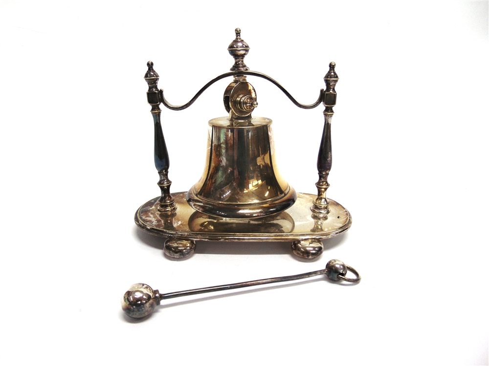A SILVER PLATED DINNER BELL the bell suspended from a frame to a base on bun feet, with striking
