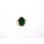 A JADE PANEL RING stamped 14K and other indistinct marks, the oval shallow cabochon claw set, finger