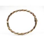 A 9 CARAT GOLD HINGED BANGLE of hollow three colour barley twist design, internal diameter 6.5cm,