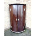 AN 18TH CENTURY MAHOGANY BOW-FRONT HANGING CORNER CUPBOARD with brass hinges and escutcheons, 63cm