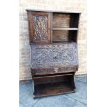 A CARVED OAK BUREAU BOOKCASE fitted with cupboard and shelf above fall front with carved Green Man