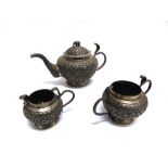 A WHITE METAL INDIAN THREE PIECE TEA SERVICE embossed profusely with flora and with Cobra handles