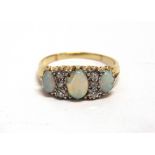 A THREE STONE OPAL RING unmarked, the graduated cabochons with trios of diamonds in between,