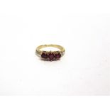 A THREE STONE RUBY RING stamped '585', with a colourless stones channel set to the shoulders, finger
