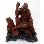 A Chinese hardwood carved figure of a bearded scholar seated on rockwork with one arm raised and