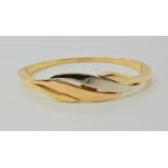 An 18ct gold three colour gold bangle of leaf form, inner dimensions 6.1cm x 5cm, weight 21.1gms