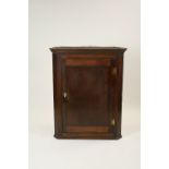 An early 19th century oak and elm straight front wall hanging corner cabinet the panel door