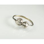 A two stone diamond crossover ring, the two brilliant cut diamonds collet set in white metal,