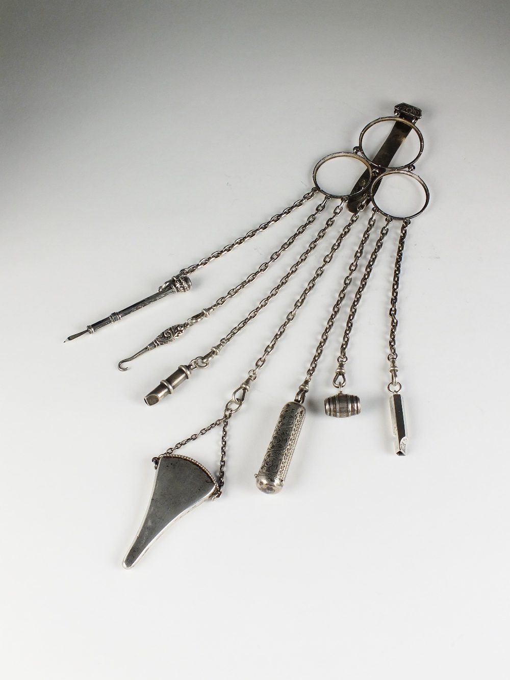 A late 19th century white metal chatelaine, suspending seven white metal and silver implements,