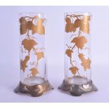 A PAIR OF ART NOUVEAU PEWTER GILT OVERLAID CYLINDRICAL VASES painted with grape vines. 19.5 cm