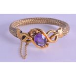 A VICTORIAN YELLOW METAL AND AMETHYST BANGLE of scrolling form.