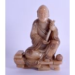 A CHINESE CARVED SOAPSTONE FIGURE OF A SEATED BUDDHA modelled holding a staff beside a censer. 15 cm