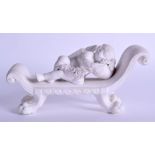 Early 19th c. hard paste biscuit figure of a sleeping cupid on a chaise lounge holding a garland